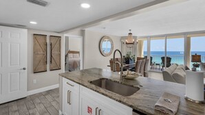 A spacious kitchen with a large island, a dining area with a view, and a balcony overlooking the ocean.