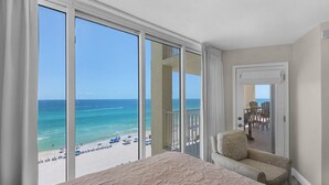 A hotel room with a large sliding glass door leading to a balcony with a beach view.