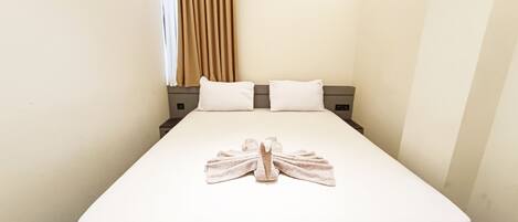 Habitación de hotel con una cama bien hecha, una toalla sobre la cama y una cortina en la ventana.