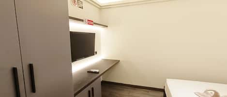 A small, well-lit room with a bed, a TV on a cabinet, and a 'No Smoking' sign.