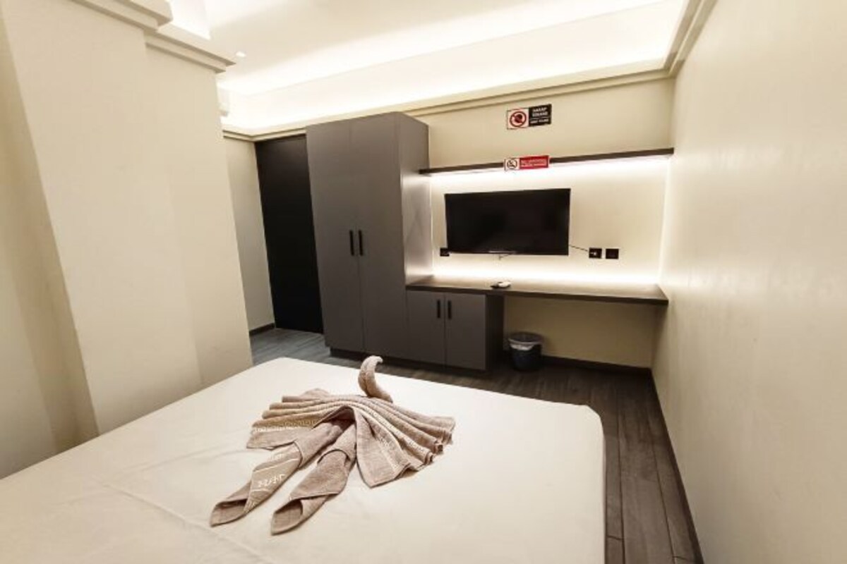 A hotel room with a bed, a TV mounted on the wall, and a small table.