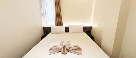 A hotel room with a neatly made bed, a window with curtains, and a wall-mounted nightstand.