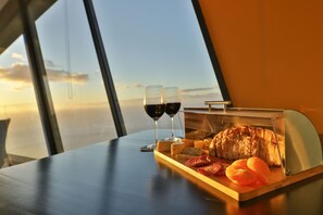 A table with a charcuterie board, two glasses of red wine, and a view of the sky through large windows. - Villa Leonor Cliffside Retreat (Calheta)