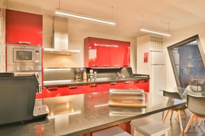 A modern kitchen with red cabinetry, stainless steel appliances, and a glass dining area.