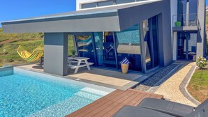 A modern house with a swimming pool, a patio with a table and chairs, and a hammock. - Villa Leonor Cliffside Retreat (Calheta)