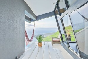 Un balcone con un'amaca, una pianta in vaso e una sedia in vimini con cuscino.