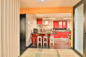 A modern kitchen with red cabinets, a marble backsplash, and a central island with stools. - Villa Leonor Cliffside Retreat (Calheta)
