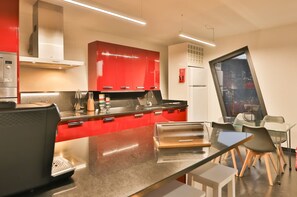 A modern kitchen with red cabinets, stainless steel appliances, and a glass dining table with chairs. - Villa Leonor Cliffside Retreat (Calheta)