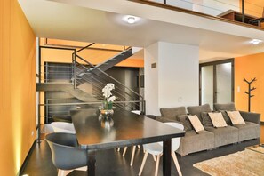 A modern living room with a dining area, a staircase, and a sofa.