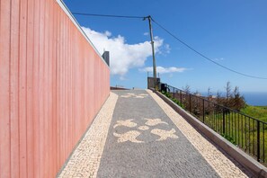 A pathway with a red wall on one side and a metal railing on the other, leading to a viewpoint with a clear sky and distant landscape. - Villa Leonor Cliffside Retreat (Calheta)