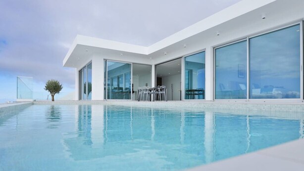 Une maison moderne dotée d’une grande piscine, de grandes portes vitrées et offrant une vue dégagée sur l’océan.