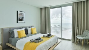 Une chambre d’hôtel moderne dotée d’un grand lit, offrant une vue sur la plage et comprenant un balcon avec des chaises longues.