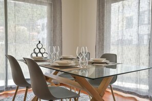 A modern dining area with a glass table, grey chairs, and a decorative metal centerpiece. - Apartamento Janela do Atlantico (Machico)