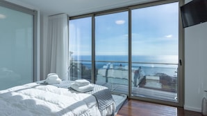 A modern bedroom with a large bed, a view of the sea, and a sliding glass door. - Villa Andrade Ocean View (Funchal)