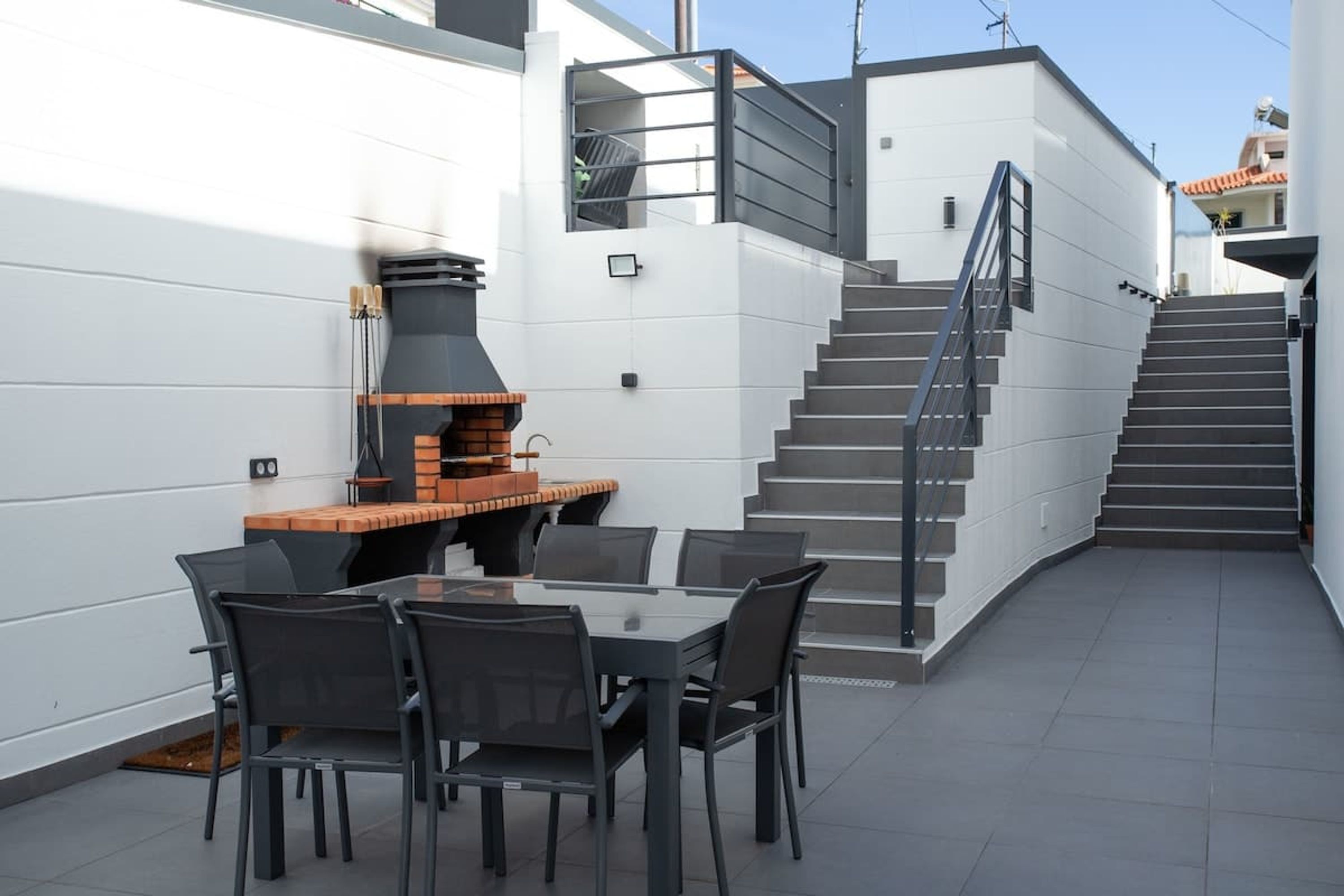 Eine moderne Außenpatio mit einem Grill, einem Esstisch mit Stühlen und einer Treppe zu einer oberen Ebene.