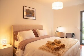 Een hotelkamer met een bed, bureau, stoel, nachtkastje en lamp.