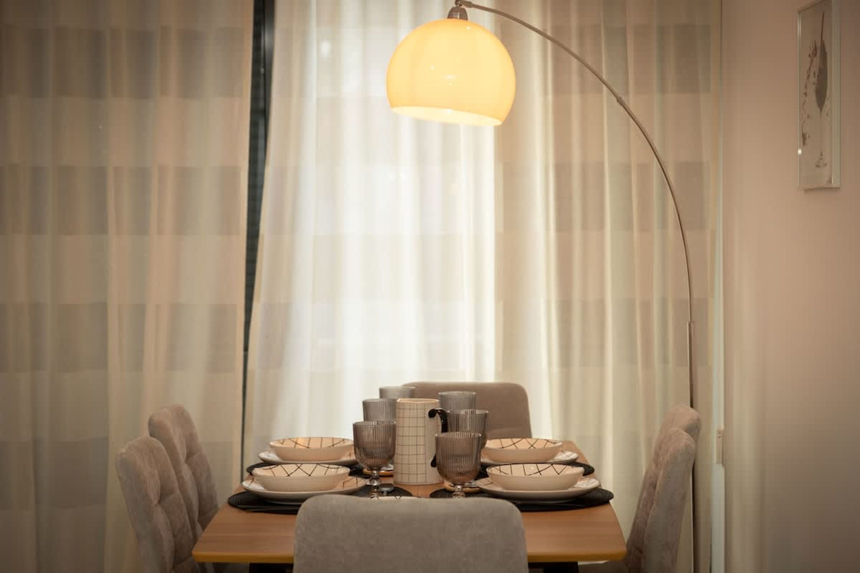 A dining table set with plates, glasses, and a pitcher, with a pendant light above.