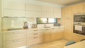 A modern kitchen with light wood cabinets, a stainless steel countertop, and built-in appliances including a microwave, toaster, and oven. - Villa Eden Nature in Prazeres (Calheta)