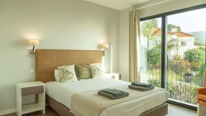 A hotel room with a bed, bedside tables, a view through a large window, and a balcony. - Villa Eden Nature in Prazeres (Calheta)