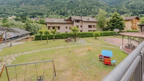 A residential area with a two-story house, a playground, and a view of a forested mountain range.