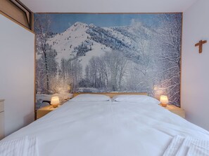 Una camera da letto con un letto grande, due comodini con lampade, una testiera in legno e un arazzo raffigurante un paesaggio montano innevato.