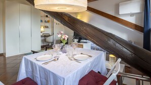 A dining area with a table set for four, a large pendant light, and a wooden beam structure. - Beautiful apartment for 2 people with A/C, WIFI and TV (Milan)