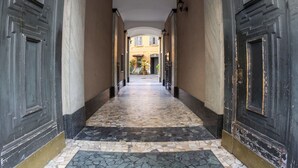 A corridor with dark wooden doors, a tiled floor, and a view into a building with a yellow facade. - Beautiful apartment for 2 people with A/C, WIFI and TV (Milan)