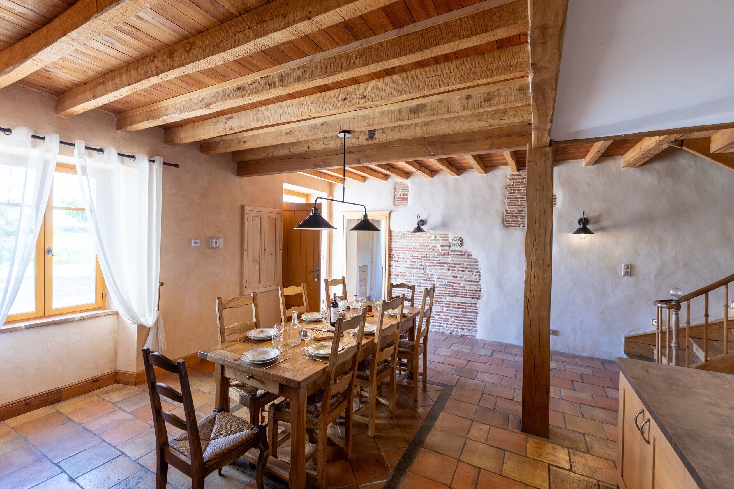A dining area with a wooden table and chairs, a brick wall, and a wooden ceiling.