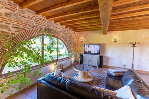 A cozy living room with a stone arch, wooden ceiling beams, a leather sofa, a coffee table, and a television.