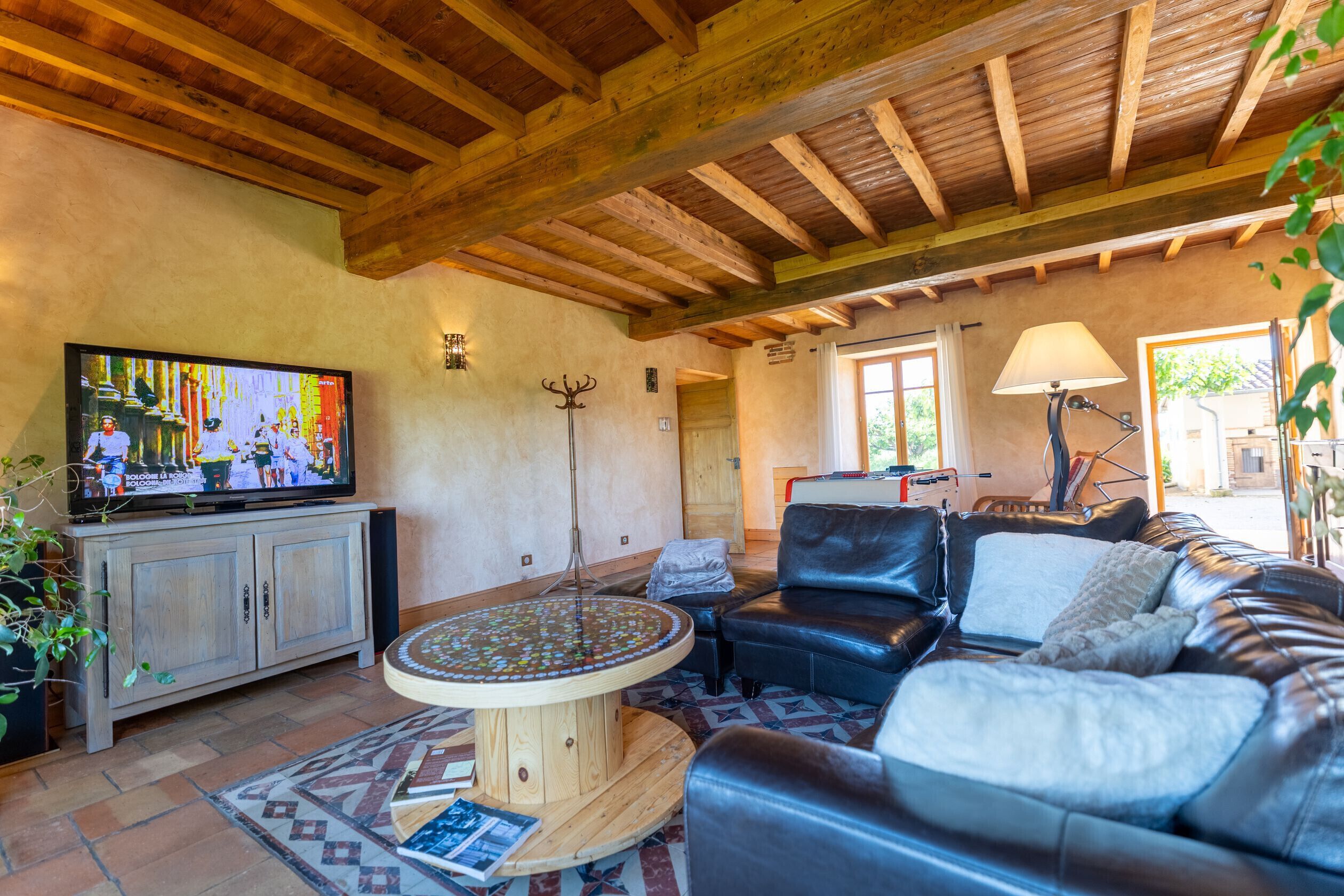 Una sala de estar con televisor, sofá de cuero, vigas de madera en el techo y una mesa de centro redonda.