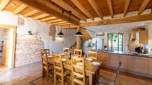 Une cuisine rustique avec des poutres en bois, un mur en briques et un coin repas comprenant des chaises et une table en bois.