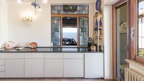 A kitchen with a central island, a chandelier, a coffee machine, and a view through a glass door. - Cosy apartment for 7 guests with WIFI, TV, terrace and pets allowed (Civitavecchia)