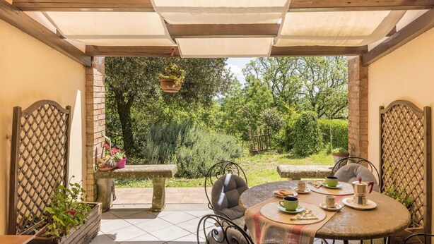 Een terras met een ronde tafel, stoelen en een hangplant.
