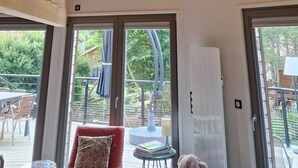 Una habitación con vigas de madera a la vista, una lámpara moderna circular, un cuadro en la pared y ventanas amplias con vistas al exterior.