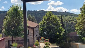 Un espacio al aire libre cubierto con vistas a una ladera boscosa, un edificio con techo rojo y una terraza de madera.
