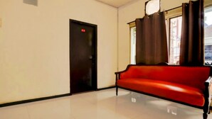 Um quarto com um sofá vermelho, uma porta preta e uma janela com cortinas.