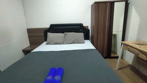 Uma cama bem arrumada com cabeceira escura, mesa de cabeceira de madeira, escrivaninha de madeira e guarda-roupa com espelho.