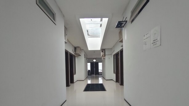 Um corredor comprido e estreito com paredes brancas e um claraboia. Há unidades de ar condicionado fixadas nas paredes e uma placa indicando a área de câmeras de segurança.