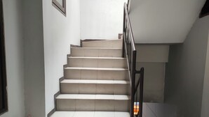 Uma escada com corrimão de metal, paredes brancas e um extintor no patamar.
