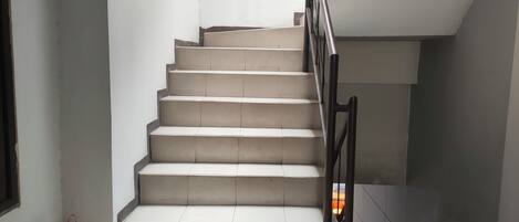 A staircase with a metal handrail, white walls, and a fire extinguisher on the landing.