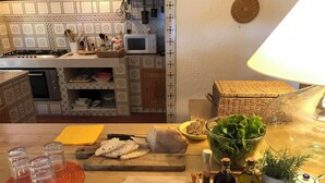 A kitchen with a microwave, stove, and various kitchen utensils. There is a cutting board with bread and a knife, a bowl of greens, and a tray with condiments.