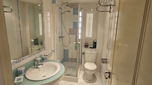Un bany modern amb una cabina de dutxa de vidre, un lavabo blanc amb taulell blau i un vàter amb tapa blanca.