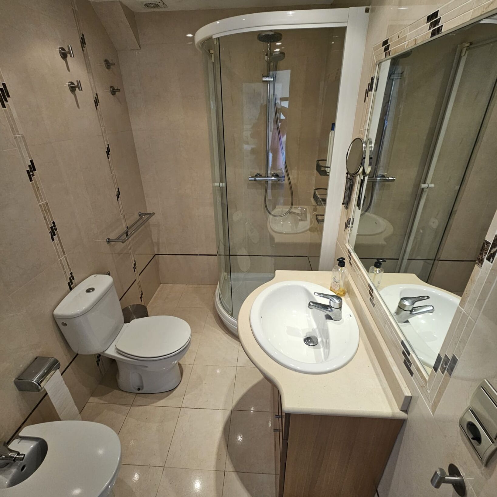 A modern bathroom with a glass-enclosed shower, a white toilet, and a sink with a mirror.