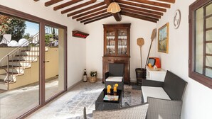Una habitación acogedora con techo de madera, una puerta de cristal que da al exterior, un sofá de mimbre, una mesita con bebidas y un armario con puertas de cristal.