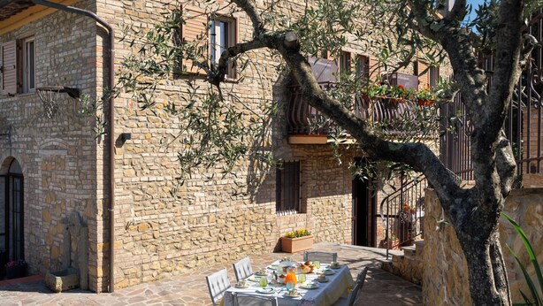 Un edificio de piedra con una mesa preparada para comer al aire libre, rodeado de vegetación.