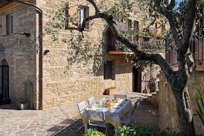 Enjoy dining al fresco under a lush tree canopy with a stone building as your backdrop.