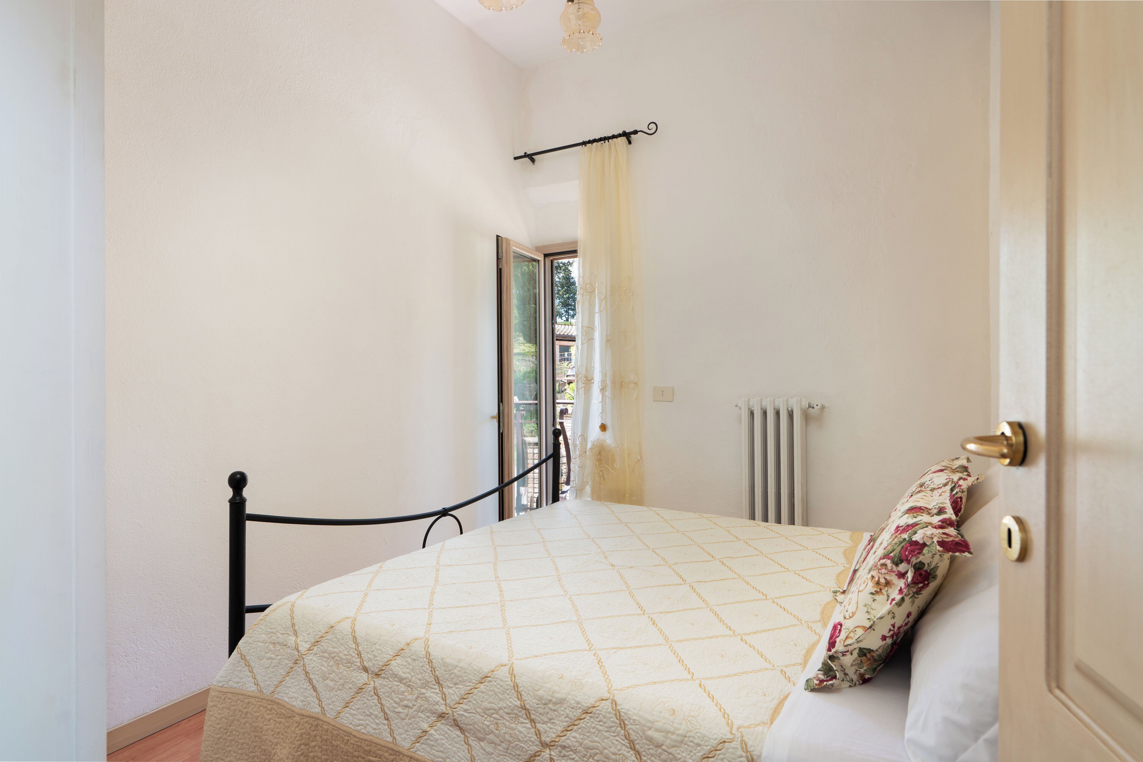 Un dormitorio con cama, una ventana con cortina, un radiador y una puerta.