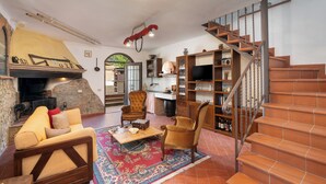 Una sala de estar acogedora con chimenea, asientos cómodos, una zona de cocina y una escalera.