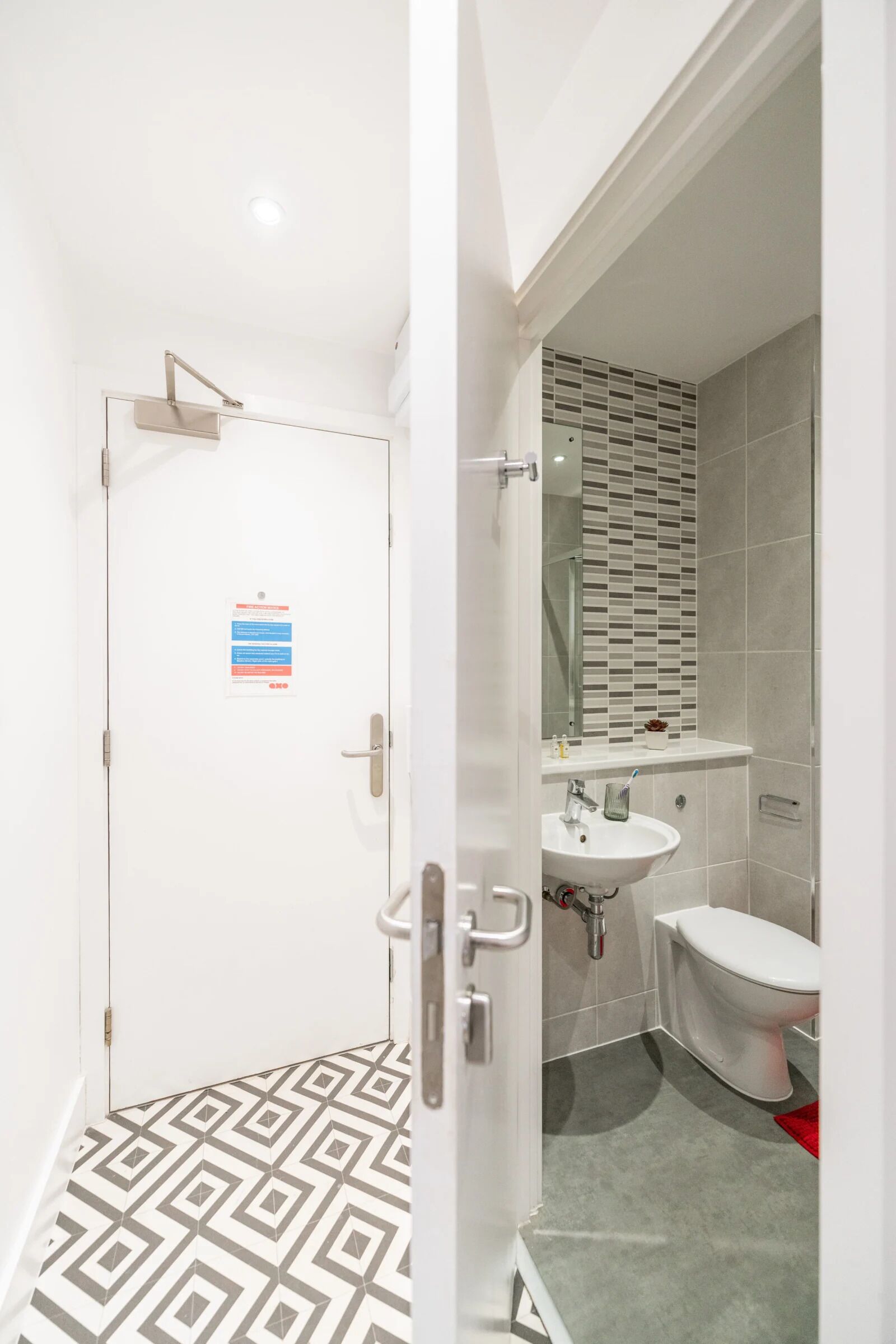 Et moderne badeværelse med et geometrisk gulvmønster, en hvid vask, et toilet og et spejl med flisebeklædt bagstykke.
