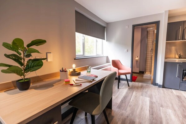 A modern kitchen with a built-in oven, a dining area with a wooden table and chairs, and a potted plant. - Sherbourne Student Village (Coventry)
